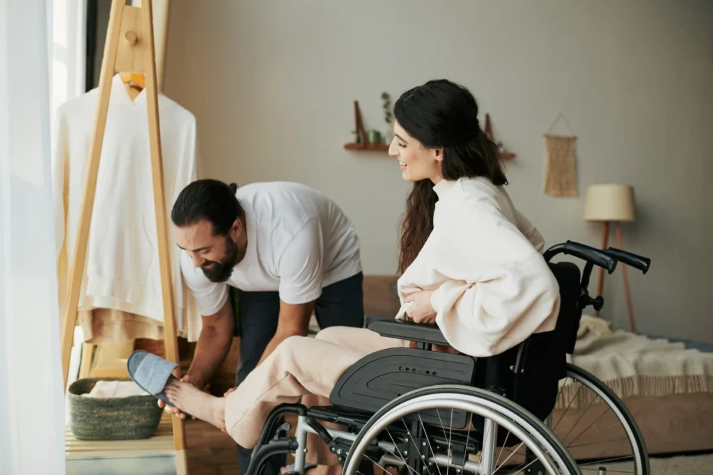 Support worker helping disabled woman in wheelchair put slippers on